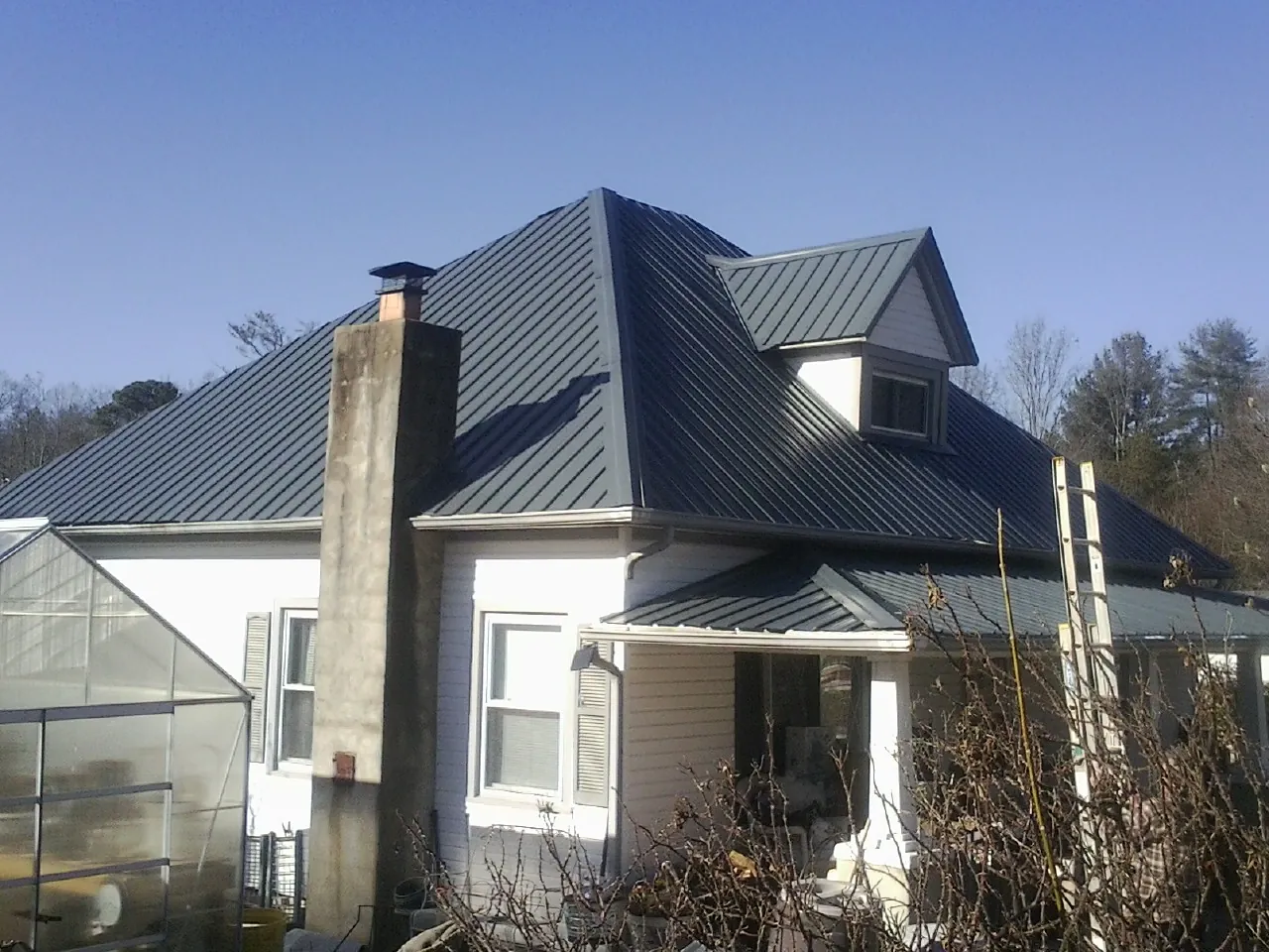 Dark blue standing seam metal roof on a white farmhouse with dormer — Slate & Tile Roof Repair by Roofing Brothers in Shawnee
