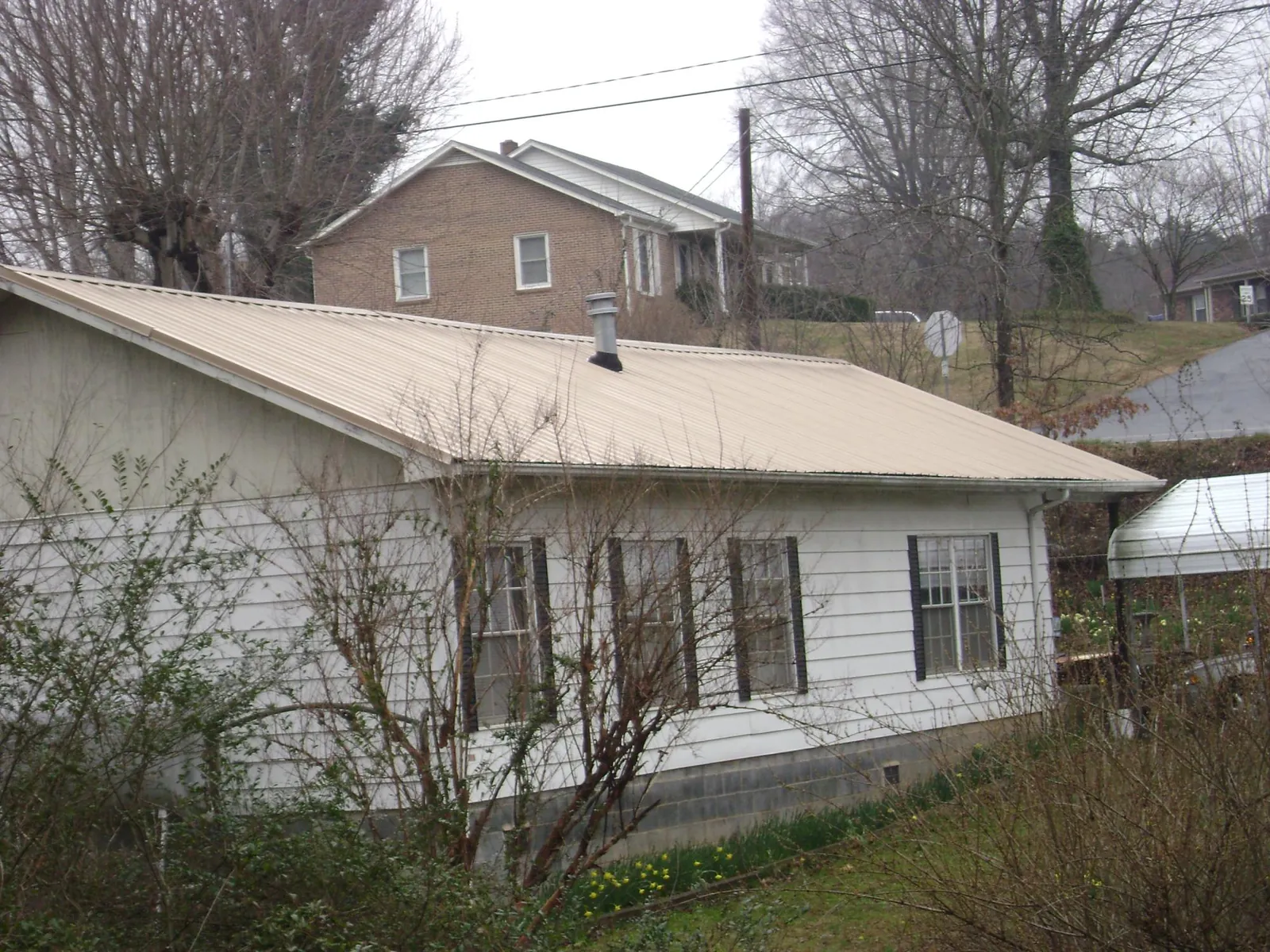 Tan metal roof on a white sided house set into a hillside — Commercial Roofing by Roofing Brothers in Shawnee