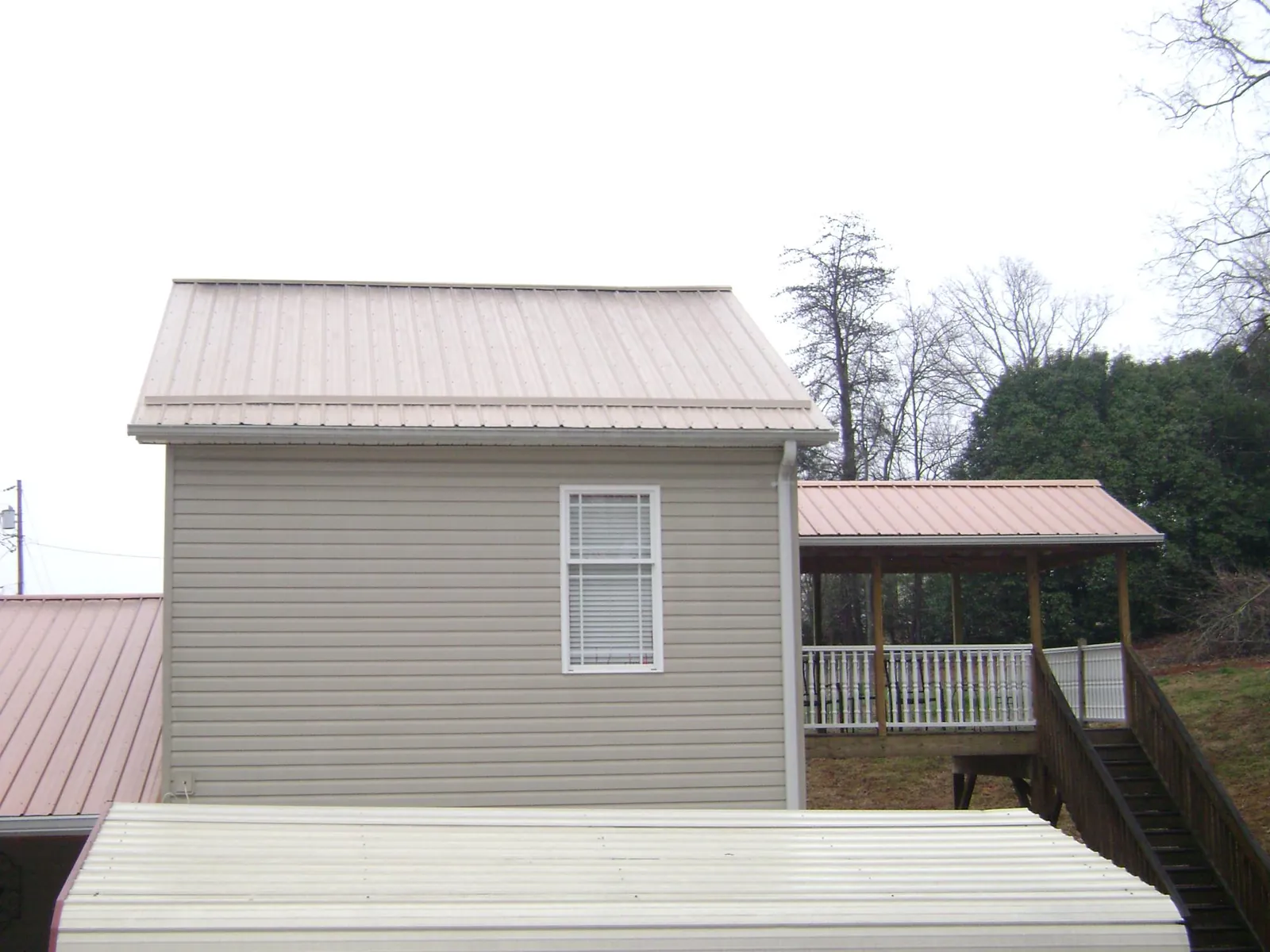 Tan metal roofs on a two story addition and attached porch, from a Roof Replacement job in Shawnee